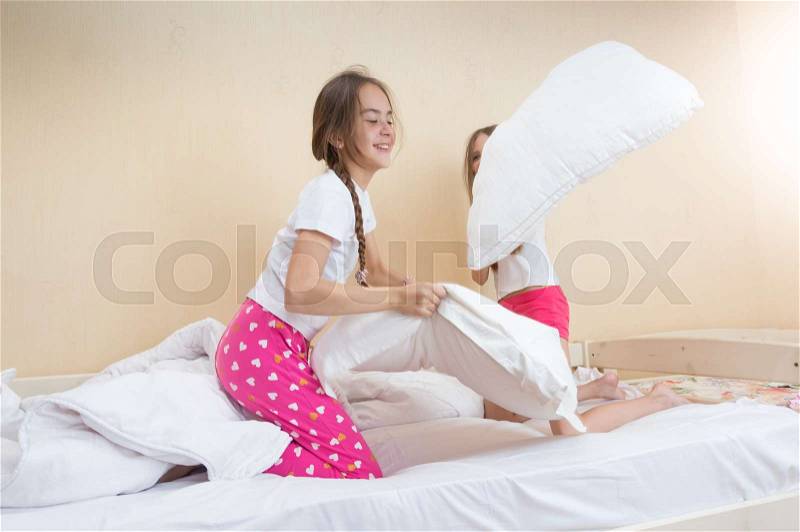 Two girls in pajamas fighting with pillows on bed, stock photo