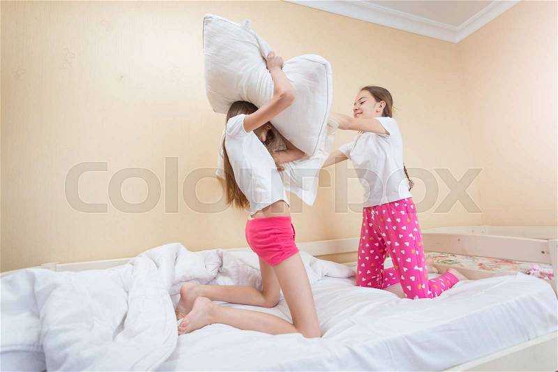 Two teenager sisters having pillow fight on bed, stock photo