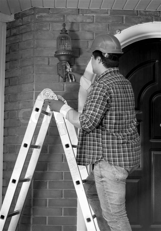 Black and white photo of electrician in helmet repairing outdoor lights, stock photo