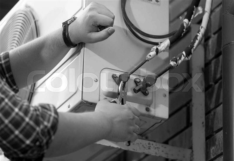 Closeup black and white photo of electrician repairing air conditioning unit, stock photo