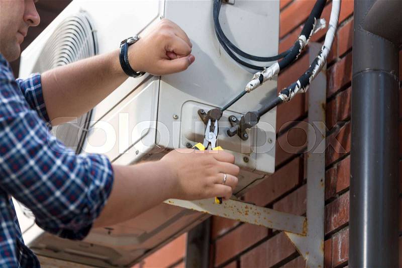 Closeup photo of male technician repairing outdoor air conditioner unit, stock photo