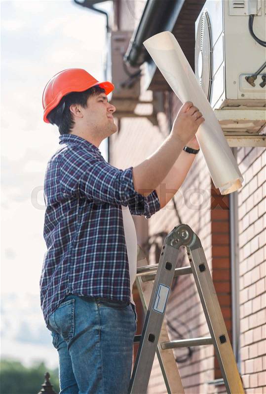 Portrait of engineer examining air conditioning system and comparing it with plan, stock photo