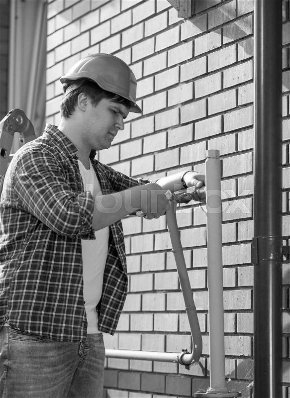 Black and white portrait of plumber assembling pipes on house outer wall, stock photo