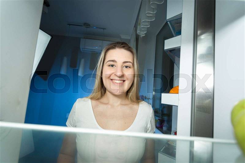 Portrait of beautiful woman in pajamas looking inside the refrigerator at home at late night, stock photo