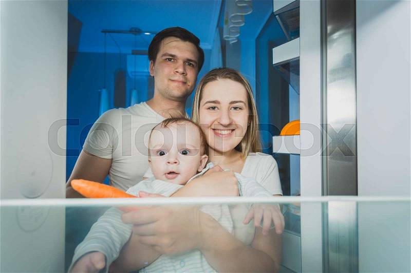 View from inside the refrigerator on smiling family looking for something to eat at late night, stock photo