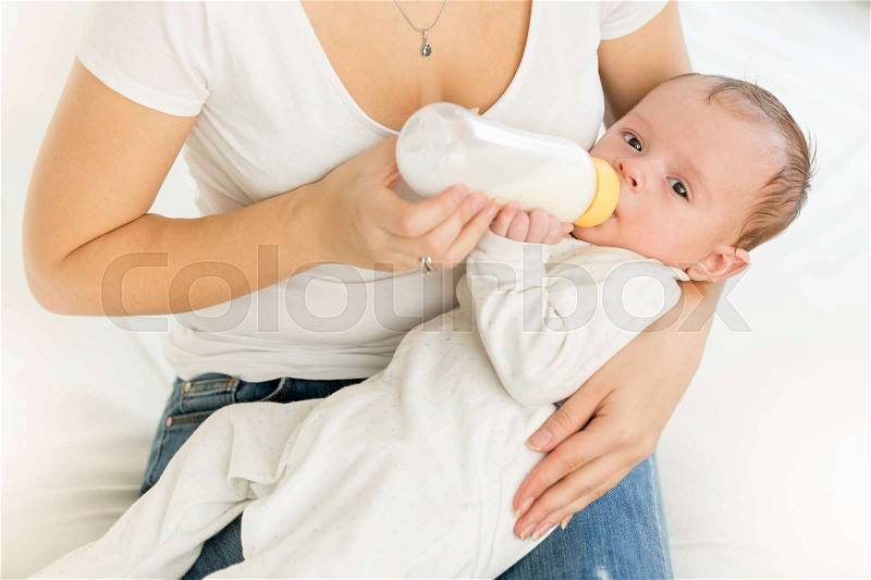 Closeup portrait of young mother holding her baby and feeding with milk from bottle, stock photo