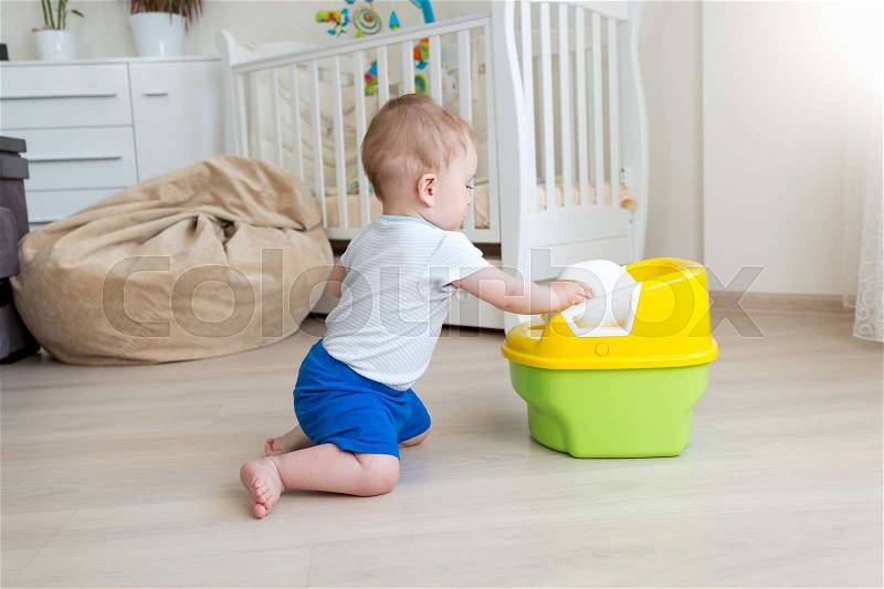 10 months old baby boy trying to sit on chamber pot at bedroom, stock photo