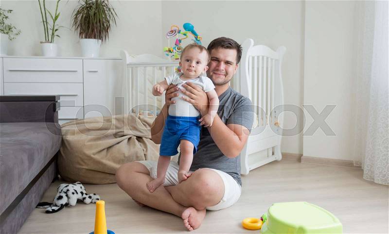 Happy young father playing with his 9 moths old baby boy on floor at living room, stock photo