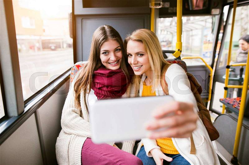 Beautiful young women traveling by bus, taking selfie with smart phone, having fun in town, stock photo