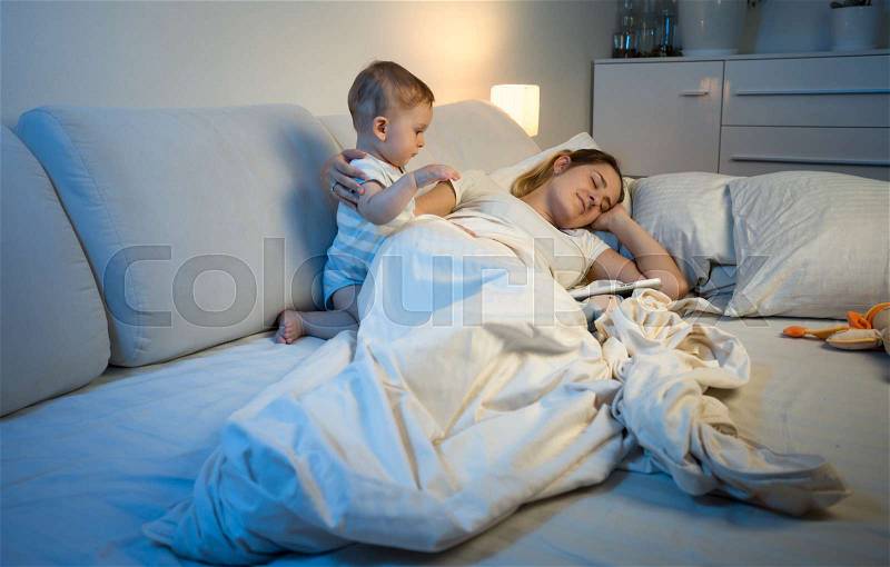 Tired mother trying to sleep while her baby waking her up, stock photo