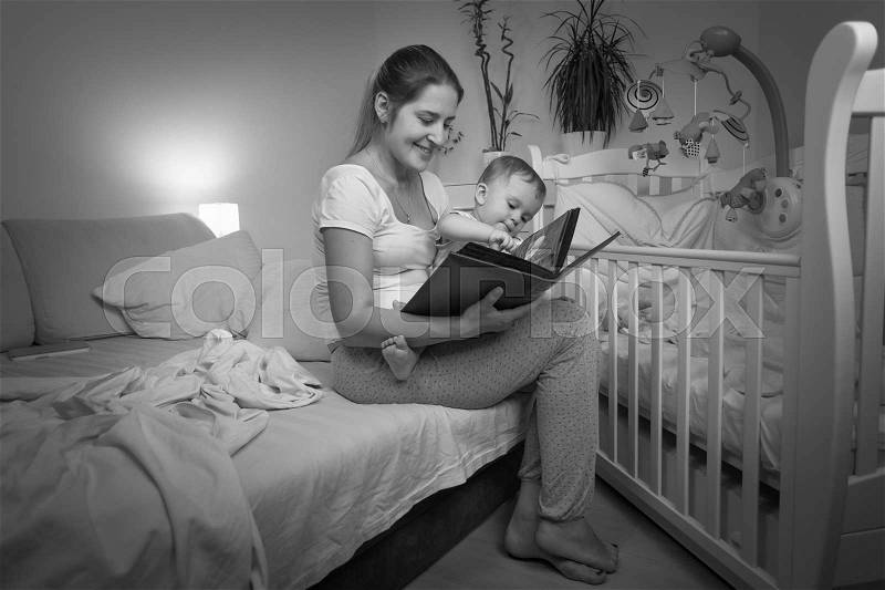 Black and white image of young mother reading book to her baby son before going to bed, stock photo