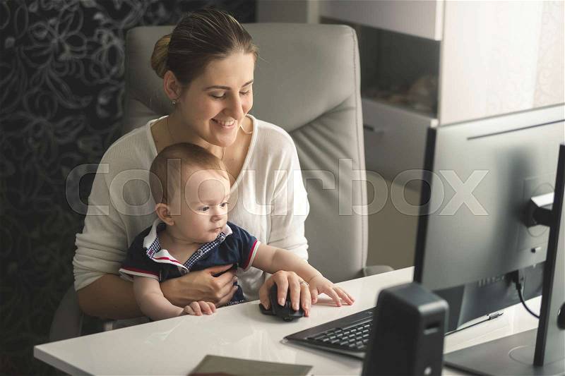 Happy smiling woman working at computer with her little baby son, stock photo