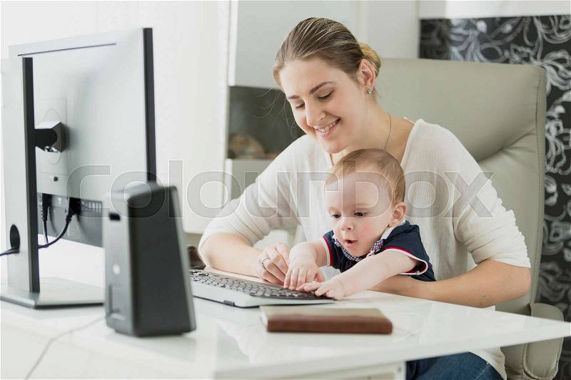 Portrait of beautiful smiling woman working on computer with her baby son, stock photo