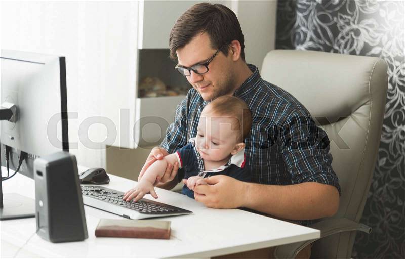 Young father working at home with his little baby boy, stock photo