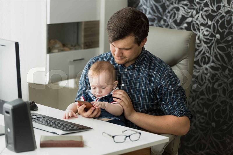Young father working from home and taking care of his baby son, stock photo