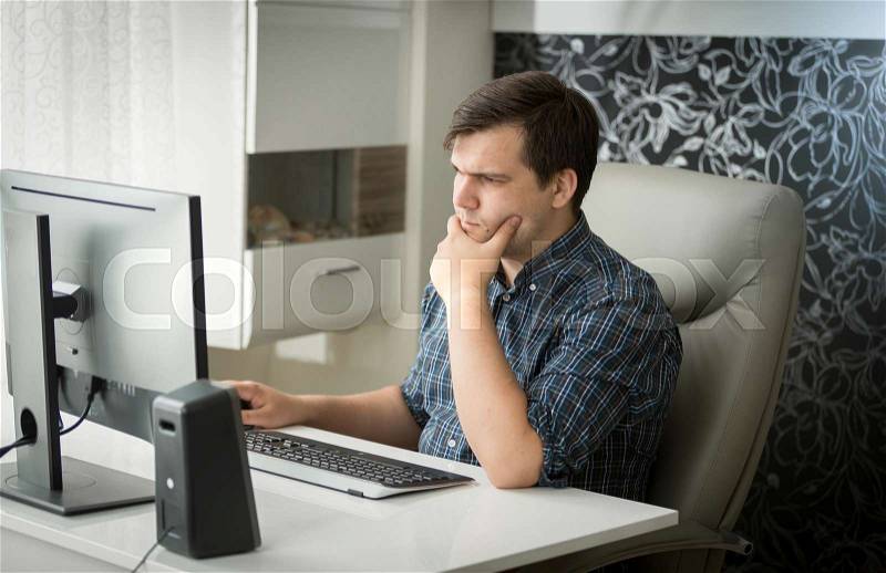 Portrait of concentrated young man working at computer, stock photo