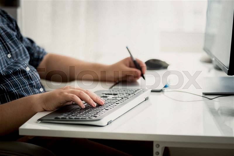 Closeup toned photo of graphic designer using tablet and keyboard at work, stock photo