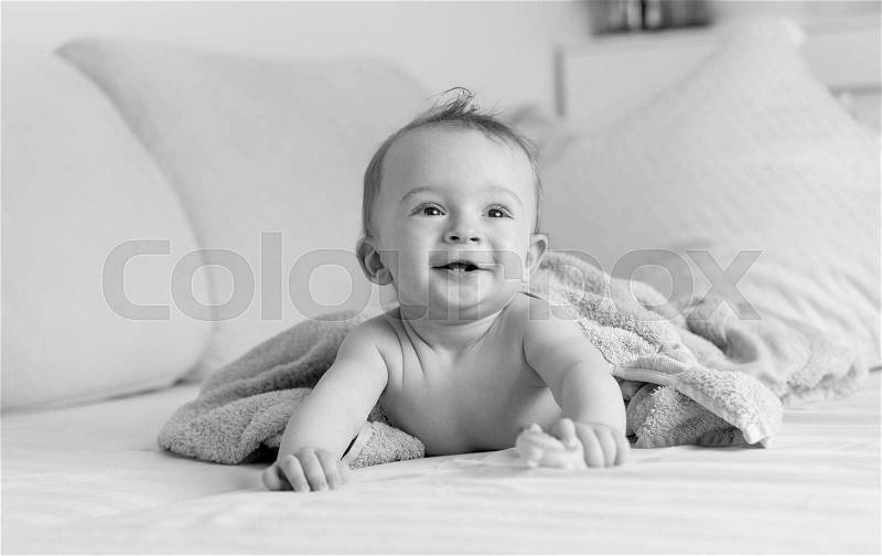 Black and white portrait of cheerful laughing baby boy lying under blanket on sofa, stock photo