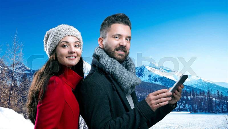 Beautiful young couple in winter clothes standing in front of winter mountains covered with snow, stock photo