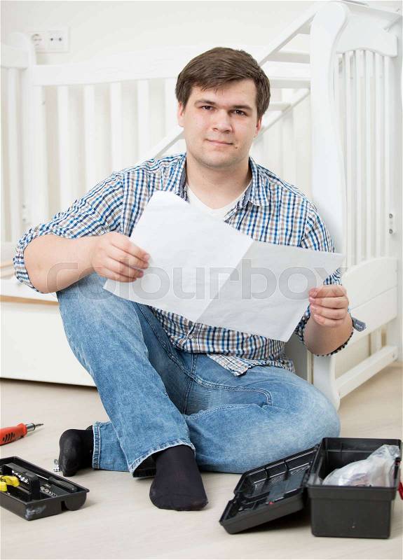Young puzzled man reading assembly instructions to baby\'s cot, stock photo