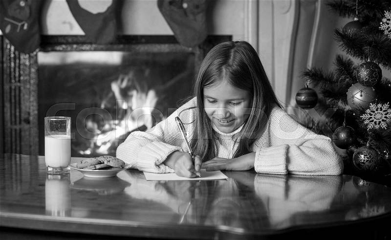 Black and white portrait of cute girl writing letter to Santa at living room, stock photo