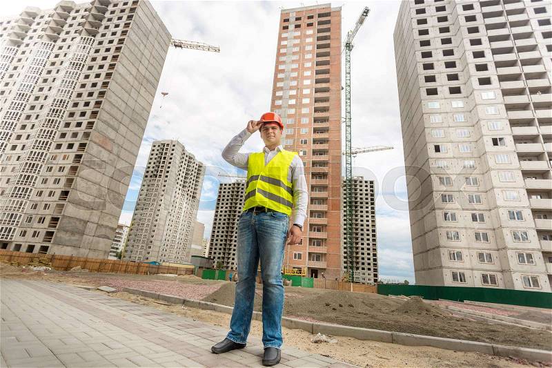Young businessman in hardhat and safety vest standing on building site, stock photo