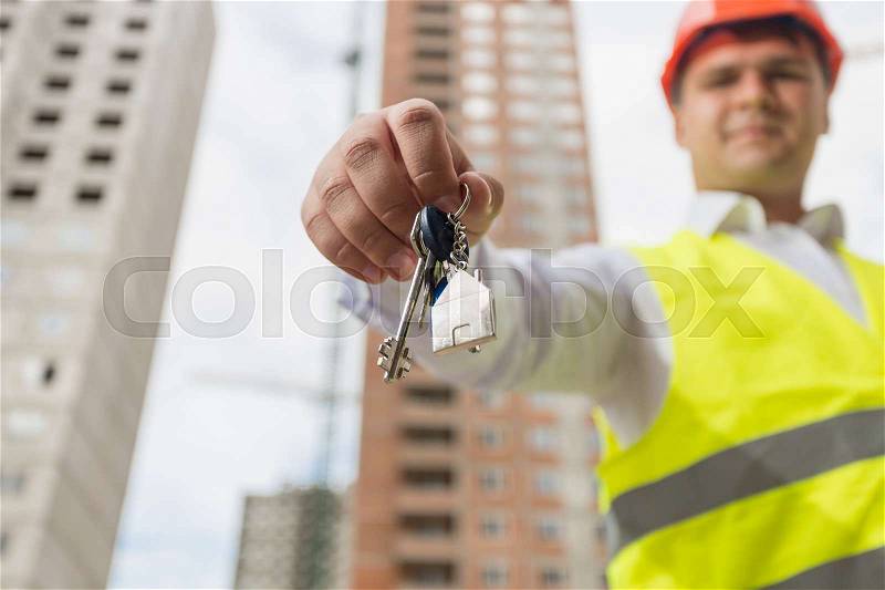Conceptual image of new home. Engineer on building site showing key from new home, stock photo