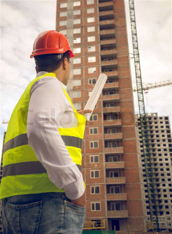 Toned photo of construction engineer pointing at building under construction, stock photo
