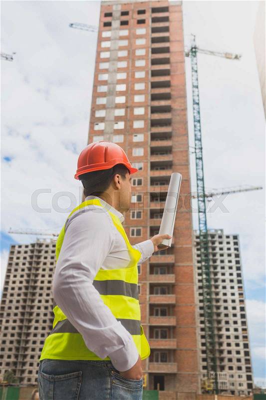 Toned image of architect in hardhat pointing at building under construction, stock photo