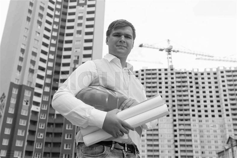 Black and white portrait of smiling engineer standing at building site, stock photo