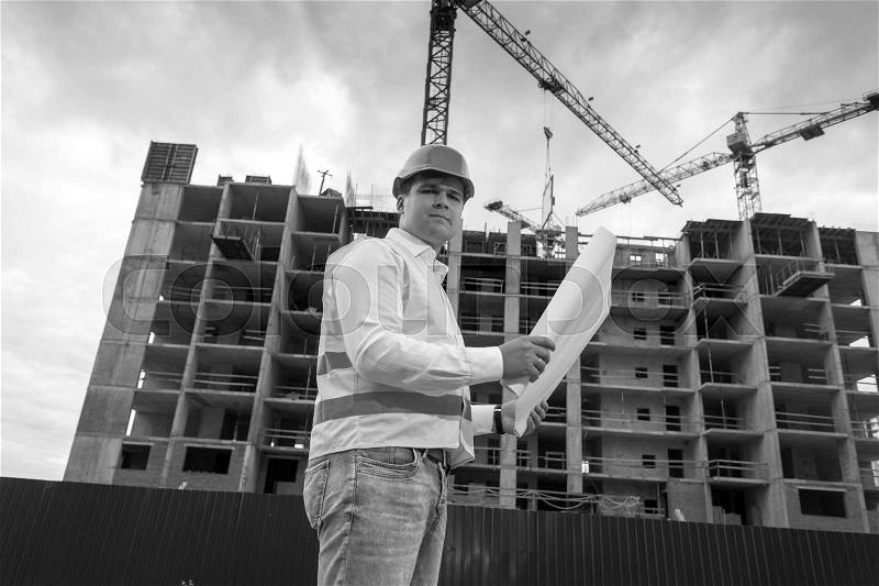 Black and white portrait of young engineer with blueprints on building site, stock photo