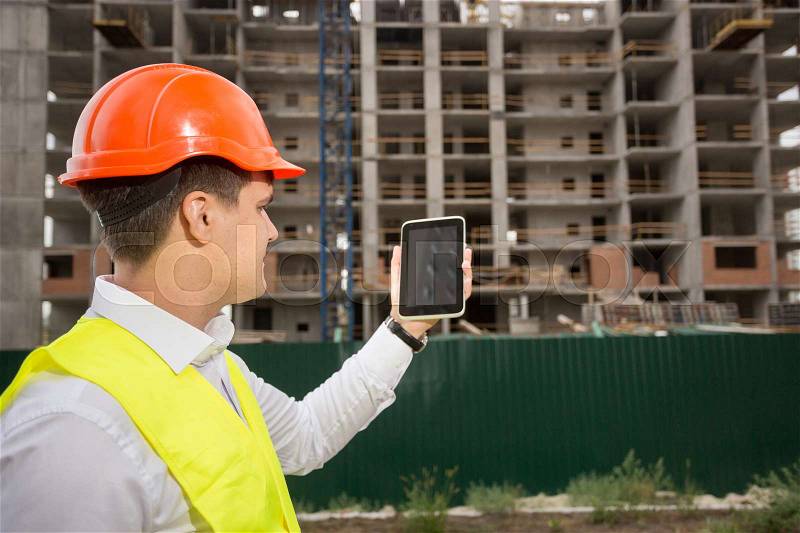 Rear view of construction engineer controlling building construction with digital tablet, stock photo