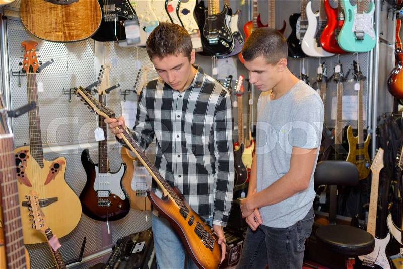 Two boys holding electric guitar in musical instrument shop, stock photo