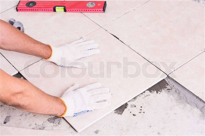 Tiler installing ceramic tiles on a floor, stock photo