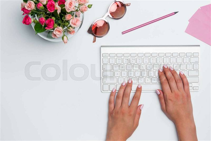 Office desk table with female hands, computer, supplies, flowers. Top view with copy space, stock photo