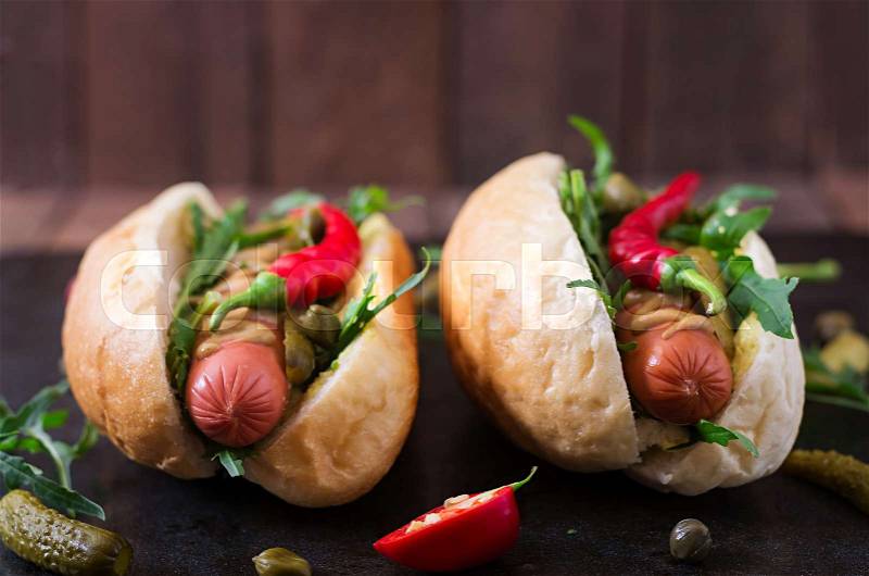 Hot dog with pickles, capers and arugula on wooden background, stock photo