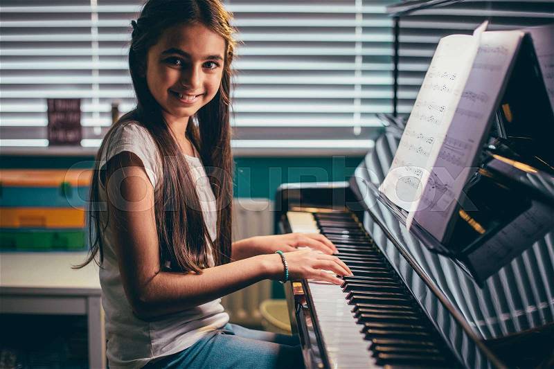 Happy girl smiling for the camera as she plays piano in her bedroom. , stock photo