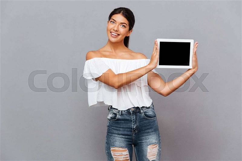 Beautiful young woman showing tablet computer with blank screen isolated on a gray background, stock photo