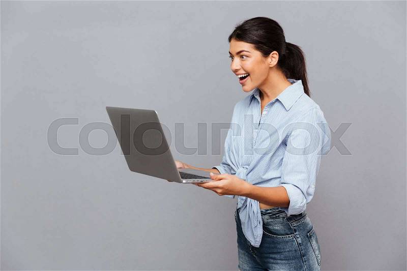 Happy beautiful excited woman using laptop isolated on a gray background, stock photo