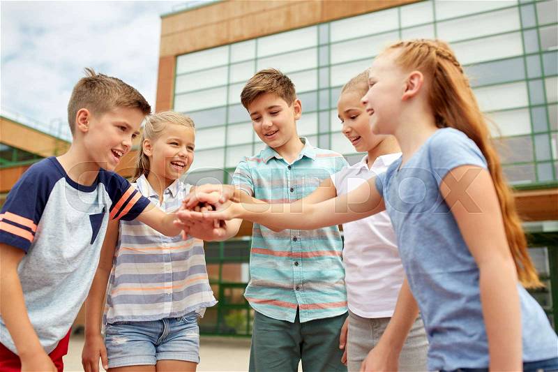 Primary education, friendship, childhood and people concept - group of happy elementary school students with hands on top outdoors, stock photo