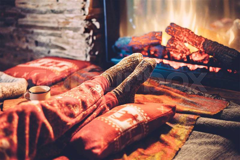 Cold fall or winter evening. People resting by the fire with blanket and tea. Closeup photo of feet in woolen socks. Cozy scene, stock photo