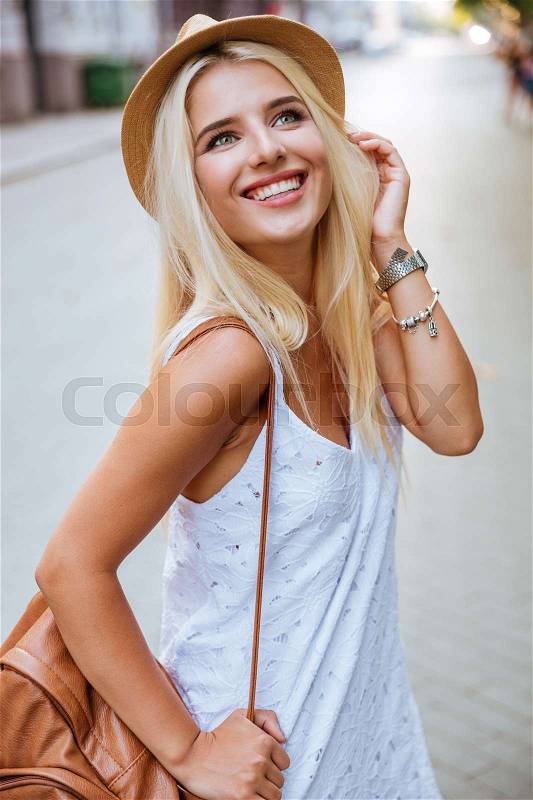 Portrait of cheerful beautiful young woman in hat standing outdoors, stock photo