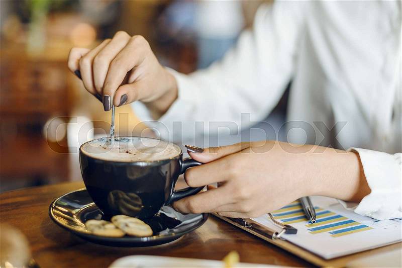 Woman stirring coffee in a cup with cookies, stock photo