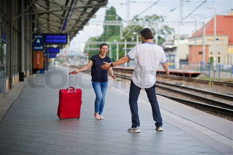 At an empty platform flee a young woman with a red suitcase. Joyful smile on her face. The young man meets her. He\'s ready to hug a woman, stock photo