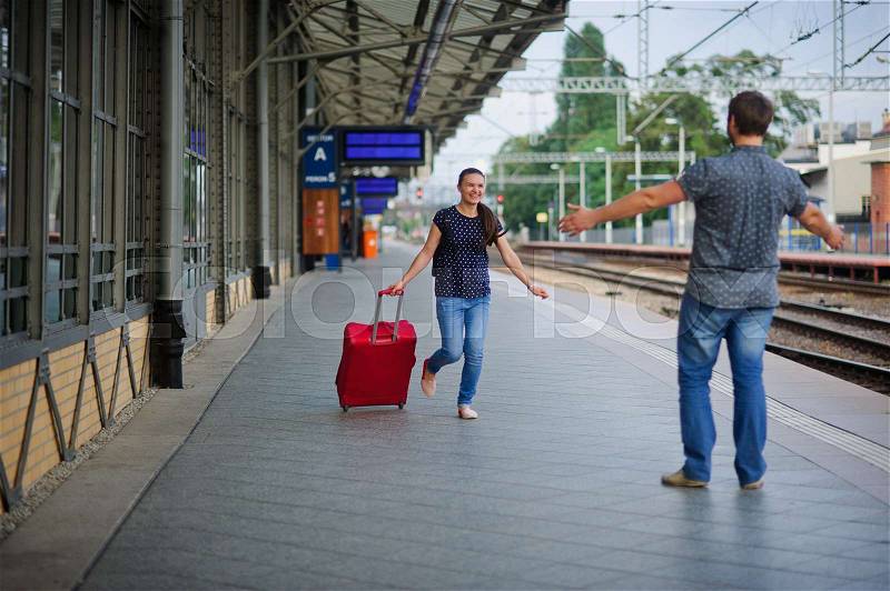 At an empty platform flee a young woman with a red suitcase. Joyful smile on her face. The young man meets her. He\'s ready to hug a woman, stock photo