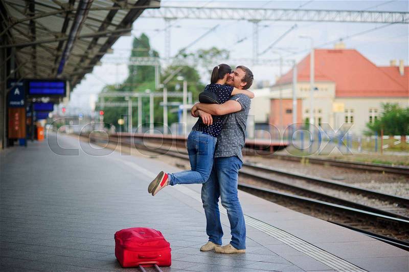 On the empty platform joyful meeting. Young man easily picked up on the hands of the girl. On his face a happy smile. Nearby is the red suitcase, stock photo
