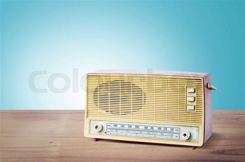 Old dusty radio from 1970 on wooden table with blue background, Vintage style, stock photo