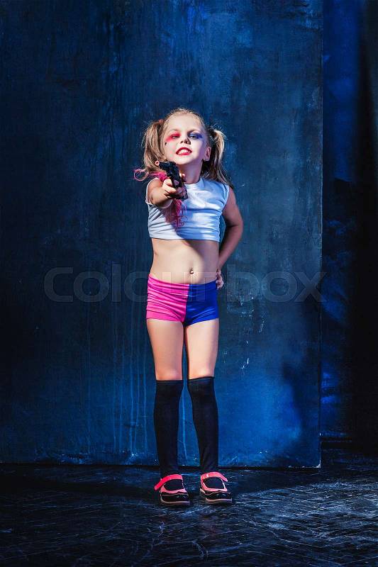 Halloween theme: Little girl pointing at toy gun on dark blue background, stock photo