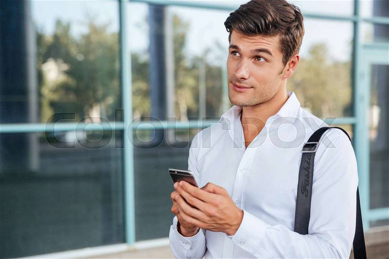 Young handsome pensive businessman using mobile phone outdoors, stock photo