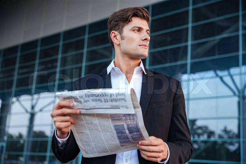 Portrait of a handsome businessman holding newspaper while standing outdoors at the office building, stock photo